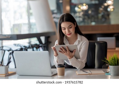 Young Asian Businesswoman Works On Tablet With Laptop At The Office.