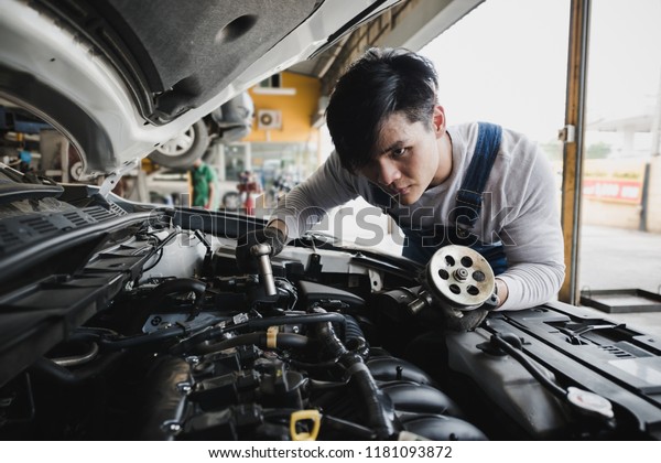 Young Asian car mechanic with spare parts working\
at service center repair