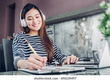 Young Asian Casual Businesswoman Listening Music And Writing Report On Office Desk,work At Home With Online E-commerce Job Concept,