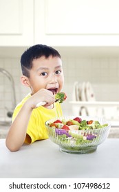 Young Asian Child Eating A Big Portion Of Salad. Shot In The Kitchen Room