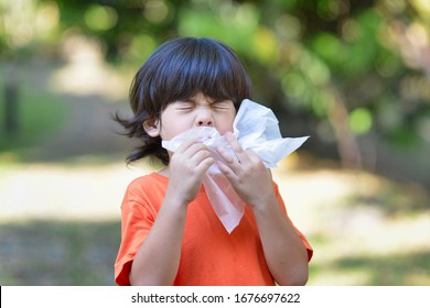 Young Asian child with virus sneezing into tissue paper.Boy allergic.Kid with flu and influenza.Corona viruses pandemic.Pollen allergy in the outdoor.