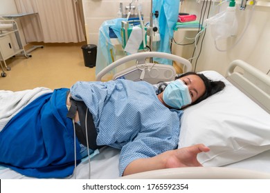 Young Asian Chinese Lady In Contraction Pain On Hospital Labour Room Ward Bed Waiting To Delivery Newborn Baby