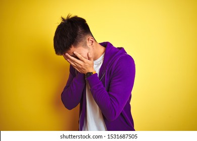 Young Asian Chinese Man Wearing Purple Sweatshirt Standing Over Isolated Yellow Background With Sad Expression Covering Face With Hands While Crying. Depression Concept.