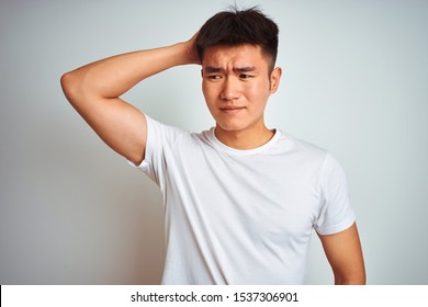 Young Asian Chinese Man Wearing T-shirt Standing Over Isolated White Background Confuse And Wondering About Question. Uncertain With Doubt, Thinking With Hand On Head. Pensive Concept.