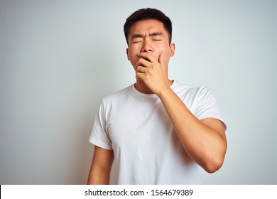 Young Asian Chinese Man Wearing T-shirt Standing Over Isolated White Background Bored Yawning Tired Covering Mouth With Hand. Restless And Sleepiness.