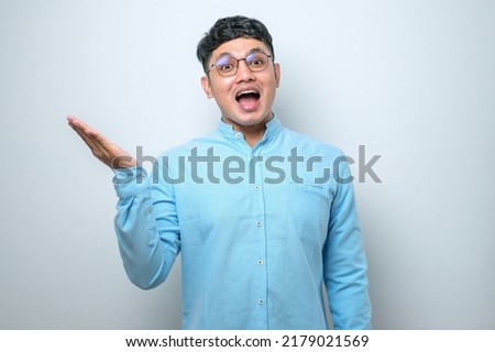 Young asian chinese man wearing casual shirt standing over isolated white background Surprised pointing with hand finger to the side, open mouth amazed expression.