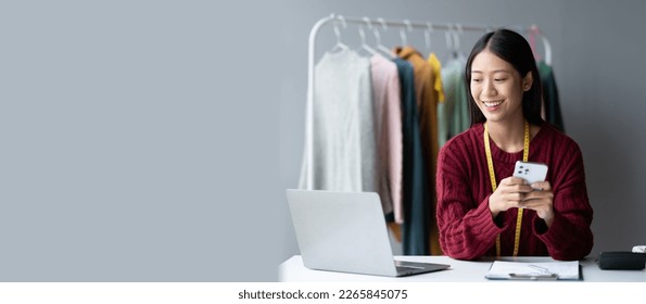 Young Asian cloth shop owner using smartphone while working in her modern studio.