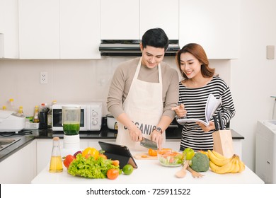 Young asian couple chopping vegetable and using digital tablet in the kitchen - Powered by Shutterstock