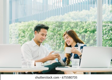 Young Asian couple, coworkers, or business partners have fun using smartphone together, with laptop computer at coffee shop. Information technology, cafe lifestyle, or romantic relationship concept - Powered by Shutterstock