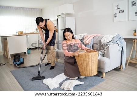 Young Asian couple doing houserkeeping together at home. Beautiful wife doing laundry and husband doing vacuum cleaning on the floor. Housework and chores concept