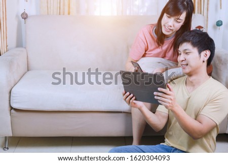 Young asian couple doing relaxing activities on sofa with laptop and smartphone at home , Focus on men. Couple relationship concept.