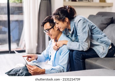 Young Asian Couple Family Having Good Time Using Technology Laptop Computer Together.Happy Couple Checking Social Media And Reading News Or Shopping Online While Sitting On At Home