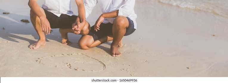 Young Asian Couple Gay Romantic Drawing Heart Shape Together On Sand In Vacation, Homosexual Happy And Fun With Love Sitting On Sand At The Beach In Travel Summer, LGBT Legal Concept, Banner Website.