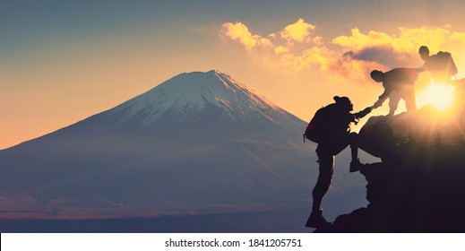 Young Asian Couple Hikers Climbing Up On The Peak Of Mountain Near Mountain Fuji. People Helping Each Other Hike Up A Mountain At Sunrise. Giving A Helping Hand. Climbing. Helps And Team Work 