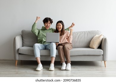 Young Asian couple with laptop gesturing YES, happy about good news, celebrating online business success, sitting on couch at home, copy space. Web lottery, internet casino win concept