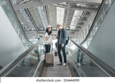 Young Asian Couple With Luggage Down The Escalator In Airport. 