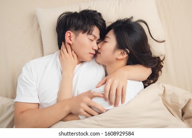 A Young Asian Couple Is Lying In Bed, Looking At Each Other, Very Close
