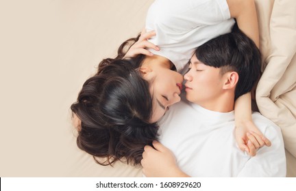 A Young Asian Couple Is Lying In Bed, Looking At Each Other, Very Close
