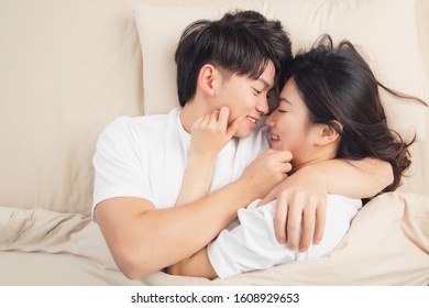 A young asian couple is lying in bed, looking at each other, very close
