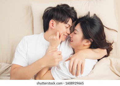 A Young Asian Couple Is Lying In Bed, Looking At Each Other, Very Close
