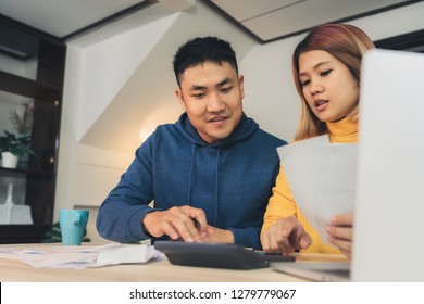 Young Asian Couple Managing Finances, Reviewing Their Bank Accounts Using Laptop Computer And Calculator At Modern Home. Woman And Man Doing Paperwork Together, Paying Taxes Online On Notebook Pc.