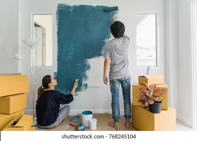 Young Asian Couple Painting Interior Wall With Paint Roller In New House, Home Decoration Concept