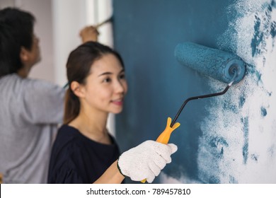 Young Asian Couple Painting Interior Wall With Paint Roller In New House, Home Decoration Concept