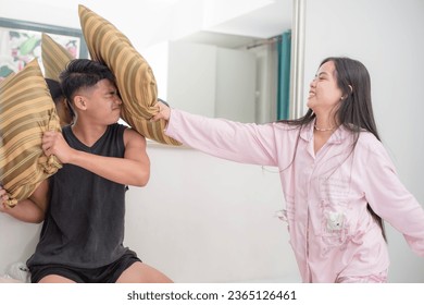 A young asian couple pillow fighting, having fun at the bedroom. A lighthearted moment in the room.