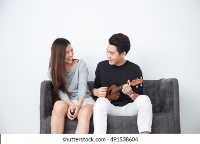 Young Asian Couple Playing Ukulele On The Couch