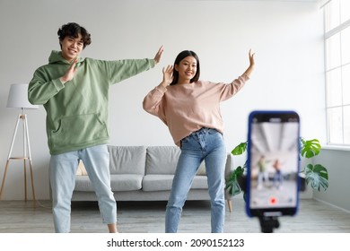 Young Asian couple recording video content, dancing on smartphone camera at home. Positive millennial boyfriend and girlfriend filming for social media, using mobile device. Vlogging concept - Shutterstock ID 2090152123