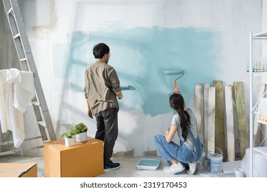 Young Asian couple repairing and painting the wall with blue paint using a roller during renovation in their new apartment. - Powered by Shutterstock