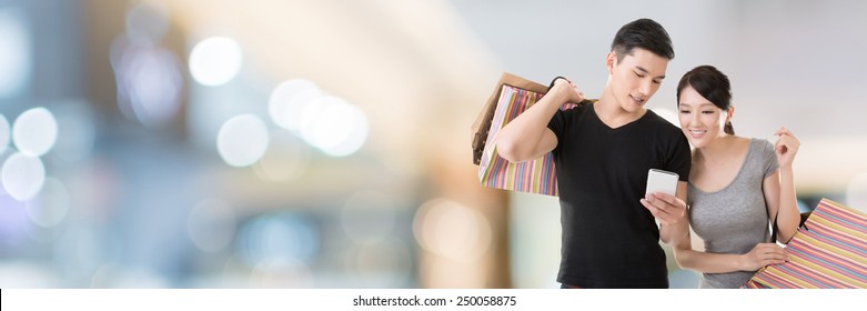 Young Asian couple shopping and looking at cellphone in the mall