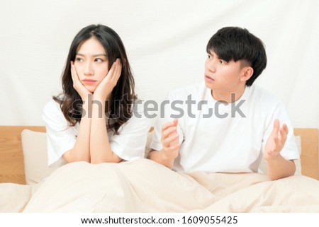 A young Asian couple sitting on a bed in short white sleeves are arguing