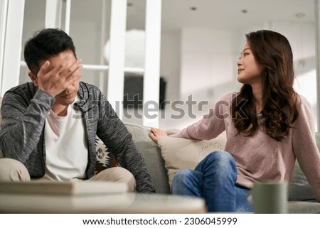 young asian couple sitting on family couch at home talking through their marriage problems