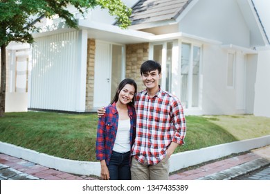 Young Asian Couple Standing In Front Of Their New House And Smiling