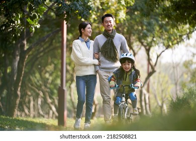 young asian couple taking a walk outdoors in park while daughter riding a kid bike happy and smiling - Powered by Shutterstock