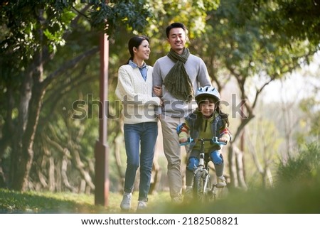 young asian couple taking a walk outdoors in park while daughter riding a kid bike happy and smiling