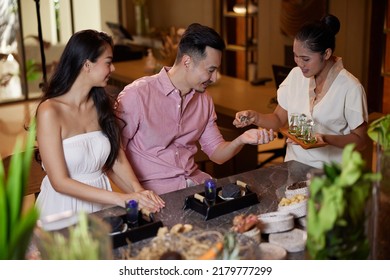 Young Asian Couple Testing Massage Oils In Luxury Beauty Salon. Spa Therapist Explains About Natural Ingredients They Use For Beauty Procedures. Weekend Date, Celebrating Honeymoon Or Anniversary.