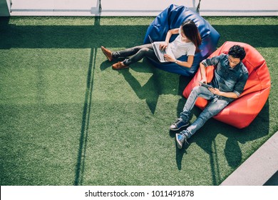 Young Asian couple using laptop notebook and digital tablet together in modern public park, sit on bean bag, top view with copy space on grass. Information technology gadget or casual business concept - Powered by Shutterstock