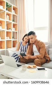 Young Asian Couple Using Laptop And Counting The Utility Bills And House Maintenance Documents