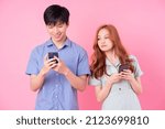 Young Asian couple using smartphone on pink background