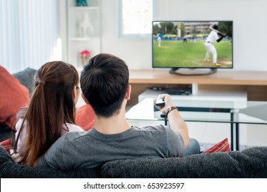 Young Asian couple waching baseball sport on tv at home