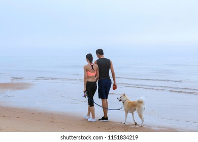 Young Asian Couple Walking Along The Coast With Pet Dog.