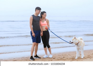 Young Asian Couple Walking Along The Coast With Pet Dog.