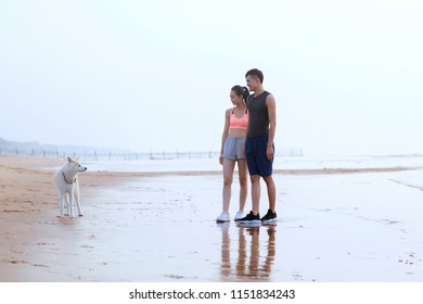 Young Asian Couple Walking Along The Coast With Pet Dog.