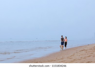 Young Asian Couple Walking Along The Coast With Pet Dog.