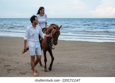 Young Asian Couple Walking With Horse On The Beach In Sunny Summer Day.