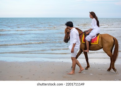 Young Asian Couple Walking With Horse On The Beach In Sunny Summer Day.