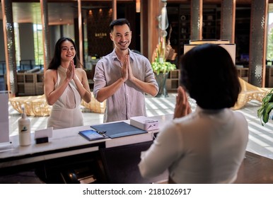 Young Asian Couple Walking In Lobby And Arriving At Hotel Reception While Front Desk Employee Welcoming And Greeting Them