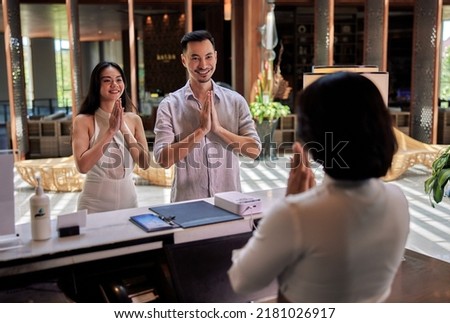 Young asian couple walking in lobby and arriving at hotel reception while front desk employee welcoming and greeting them